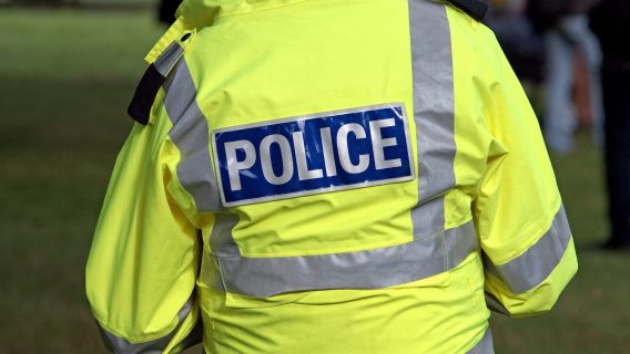 Image shows a police officer wearing a yellow jacket which says 'police' on it.