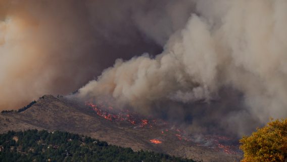 Image shows a wildfire on a hillside and smoke.